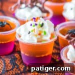 Purple and orange layered Halloween Jello Shots topped with whipped cream and sprinkles.