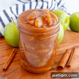 Apple pie filling in a wide mouth mason jar with cinnamon sticks and apples around it.