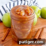 Apple pie filling in a wide mouth mason jar with cinnamon sticks and apples around it.