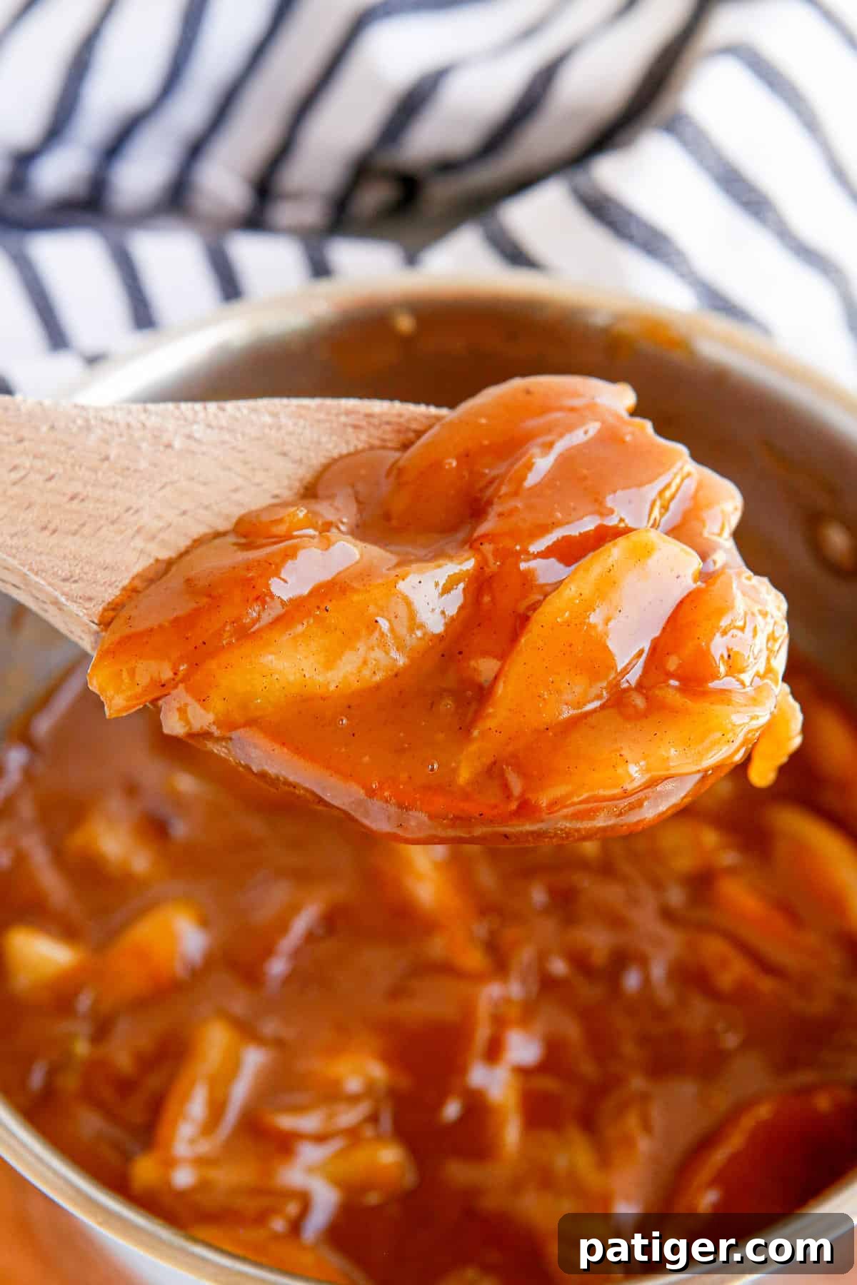 Wooden spoon lifting apple pie filling out of pot.