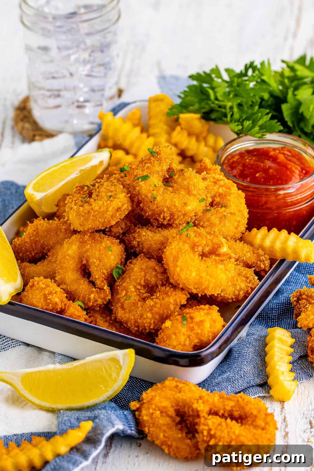 Panko breaded fried shrimp served with cocktail sauce, lemon wedges, and french fries. A plate piled high with crispy shrimp, golden fries, a bowl of zesty cocktail sauce, and bright lemon wedges, ready to be enjoyed.