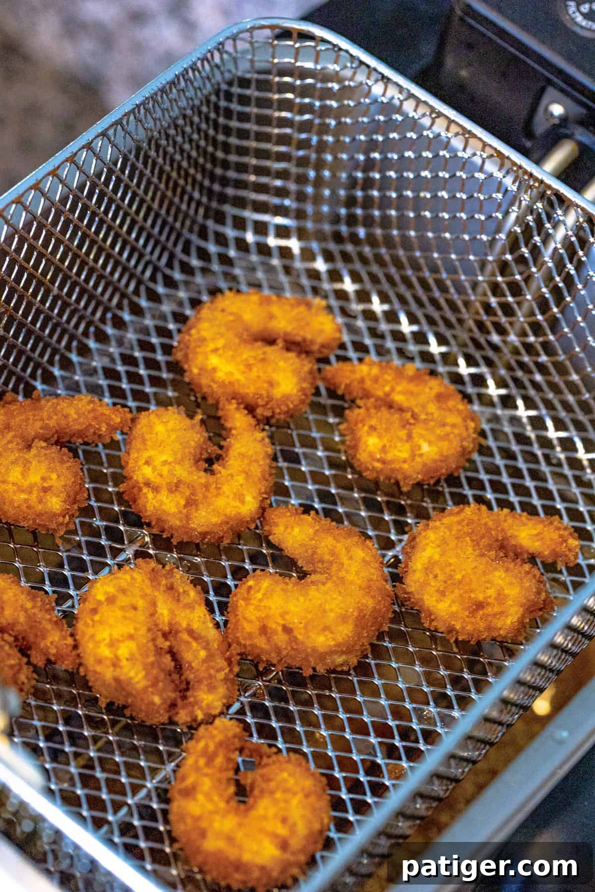A deep fryer basket lowered into hot oil, frying several panko-coated shrimp to golden perfection.