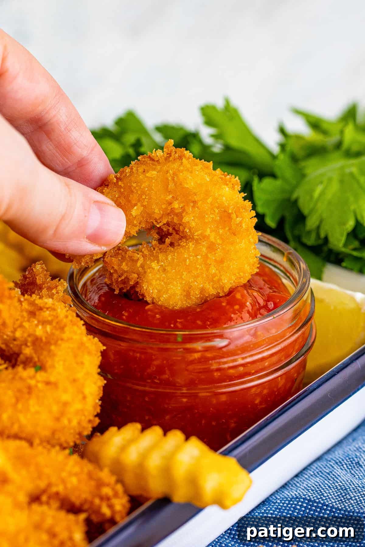 A hand dipping a crispy panko fried shrimp into a bowl of cocktail sauce.
