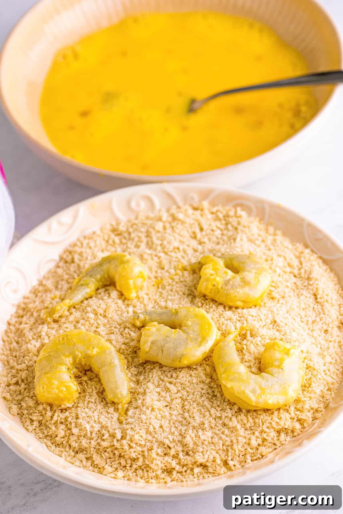 A hand gently pressing panko breadcrumbs onto an egg-washed shrimp, ensuring full coverage.