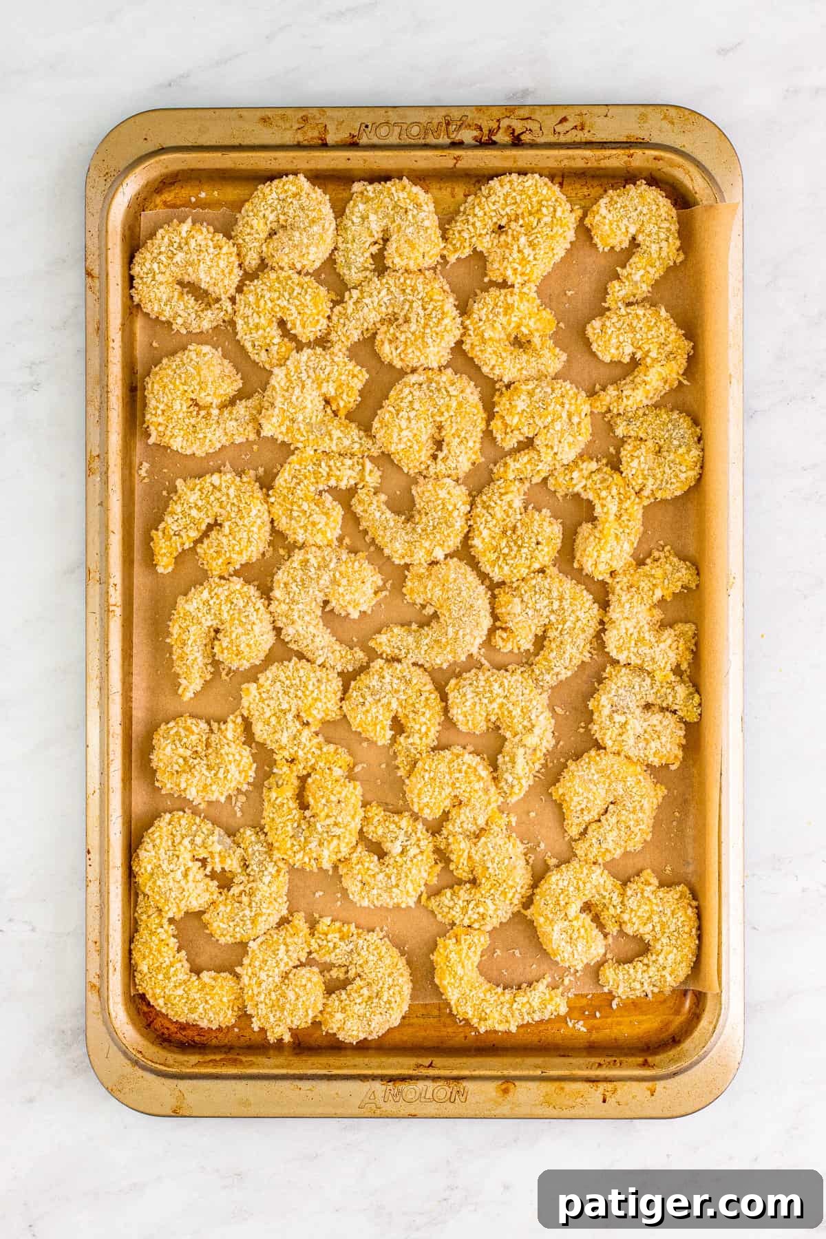 A sheet pan lined with parchment paper, holding several perfectly panko-breaded shrimp, ready for frying.