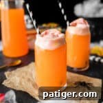 Hocus pocus punch - an orange drink topped with rainbow sherbet and a black and white paper straw.