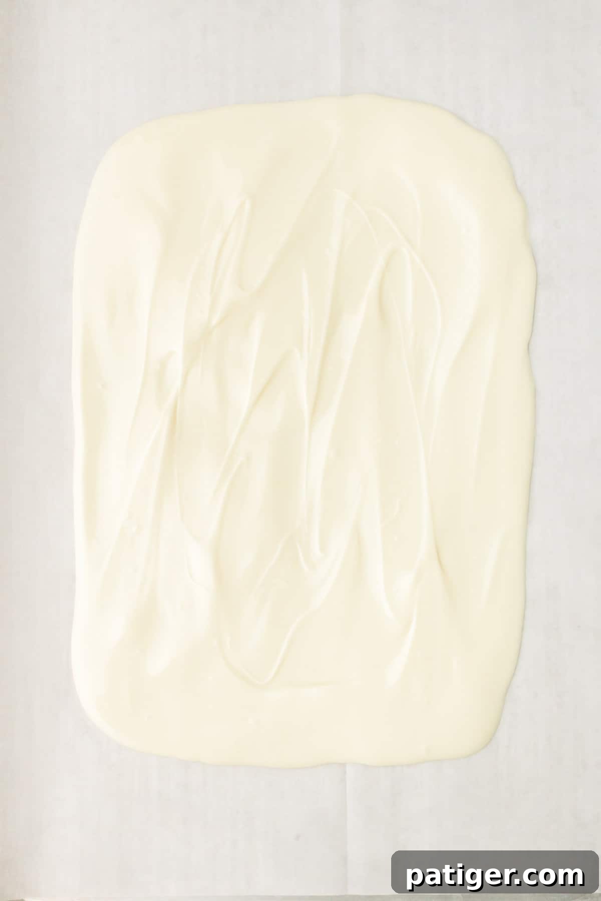 Melted white candy spread into even layer on lined baking sheet.