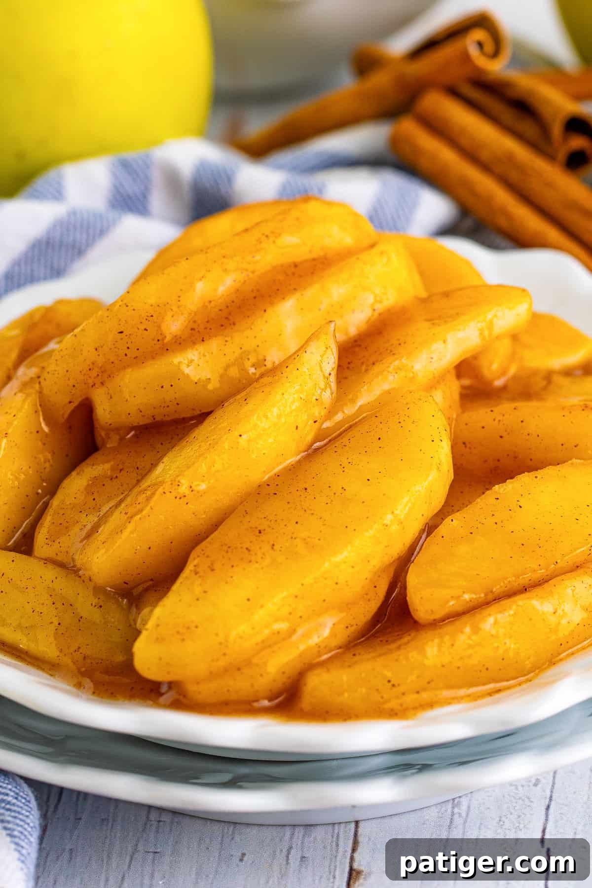 Copycat Cracker Barrel Fried Apples on white plate with fresh apples, cinnamon sticks, and orange juice in background.
