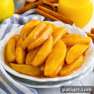 Copycat cracker barrel fried apples served on white plate with cinnamon sticks and juice next to them on the table.