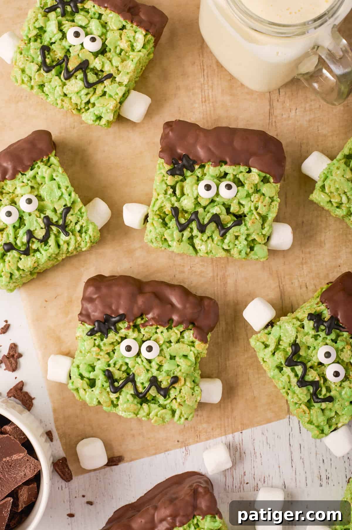 Spooktacular Frankenstein Krispies 2 Cute frankenstein rice krispies treats on a piece of parchment paper with mini marshmallows scattered and a glass of milk.