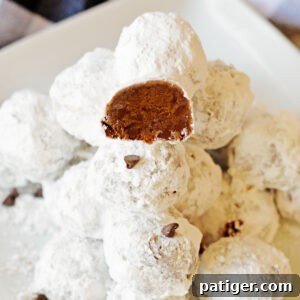 Double chocolate snowball cookies stacked on a white plate with one cookie cut in half to show chocolate interior packed with mini chocolate chips.