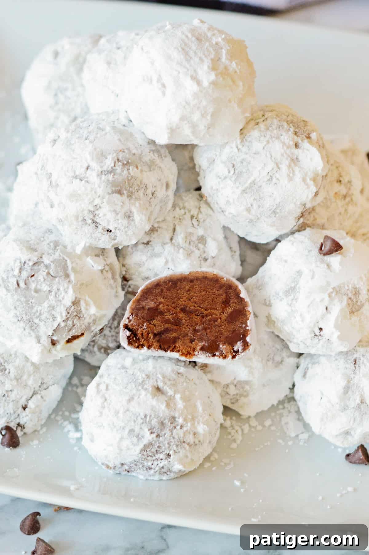 Chocolate snowballs on white plate with one cookie cut in half.