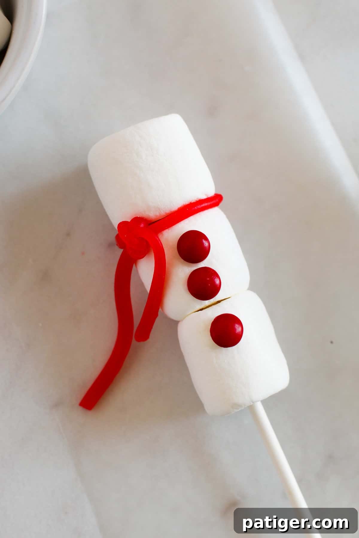 A festive red candy strand tied between the top and middle marshmallows, forming a charming snowman scarf.