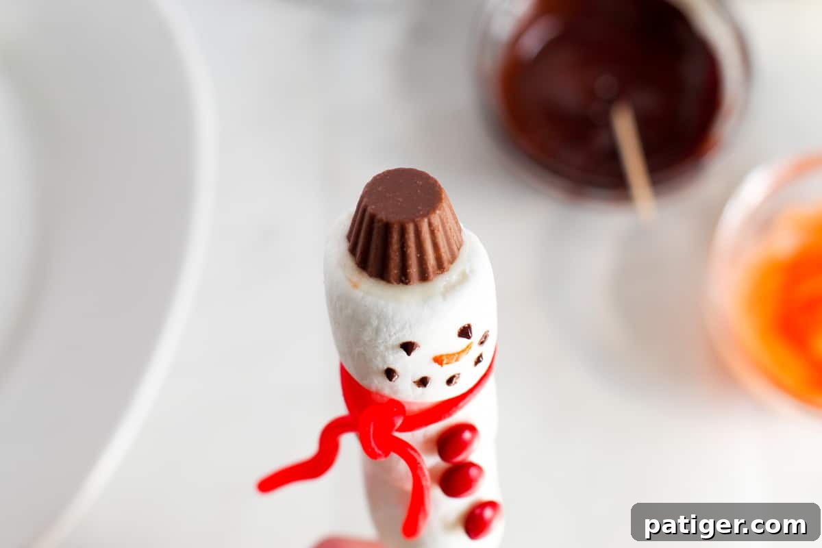 A mini peanut butter cup, inverted and secured with frosting, placed atop the snowman pop as a hat.