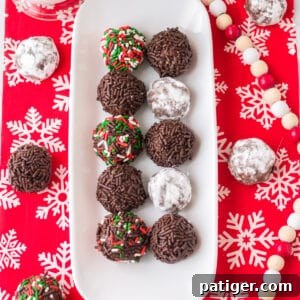 Chocolate rum balls coated in powdered sugar or sprinkles and on a white serving tray over a holiday table cloth.