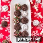 Chocolate rum balls coated in powdered sugar or sprinkles and on a white serving tray over a holiday table cloth.