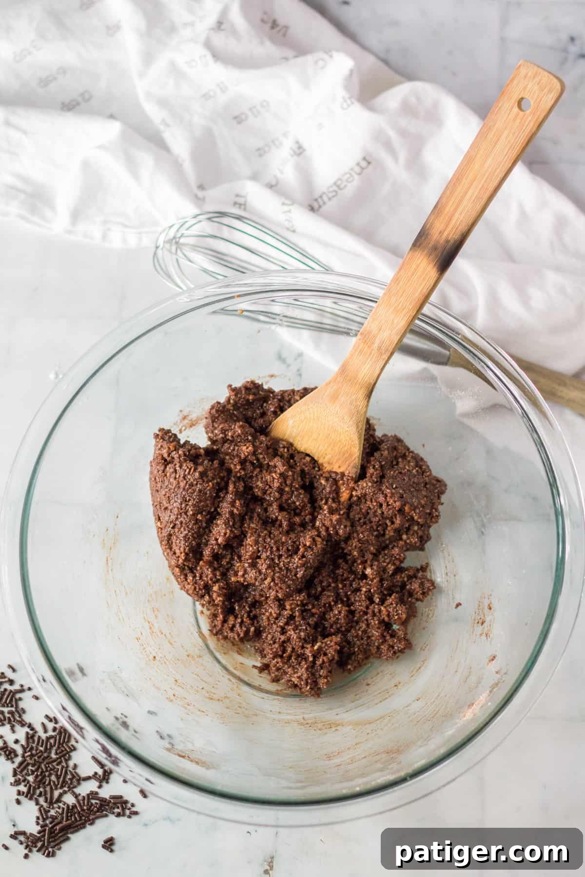 Rum ball dough in glass mixing bowl with wooden spoon.