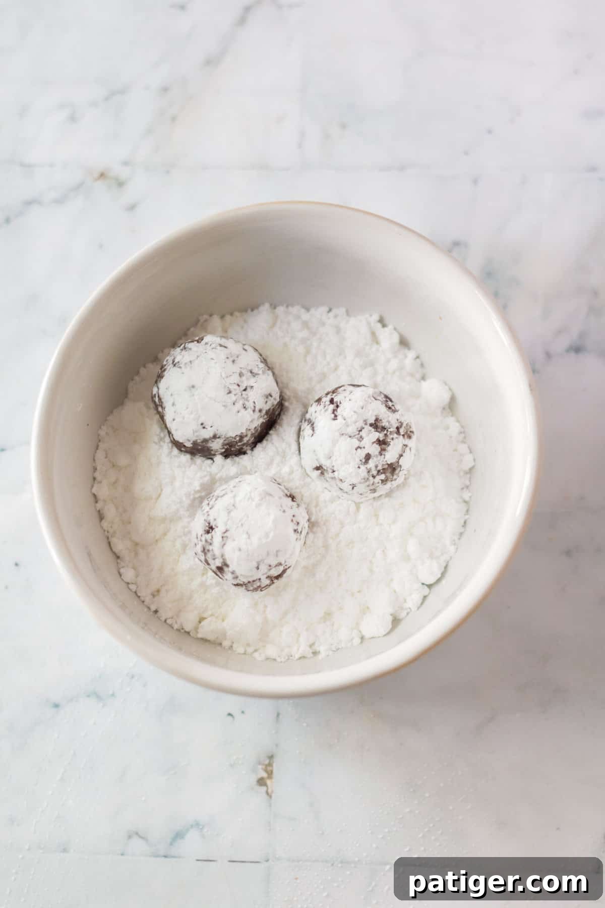 Rum balls being rolled in bowl of powdered sugar.