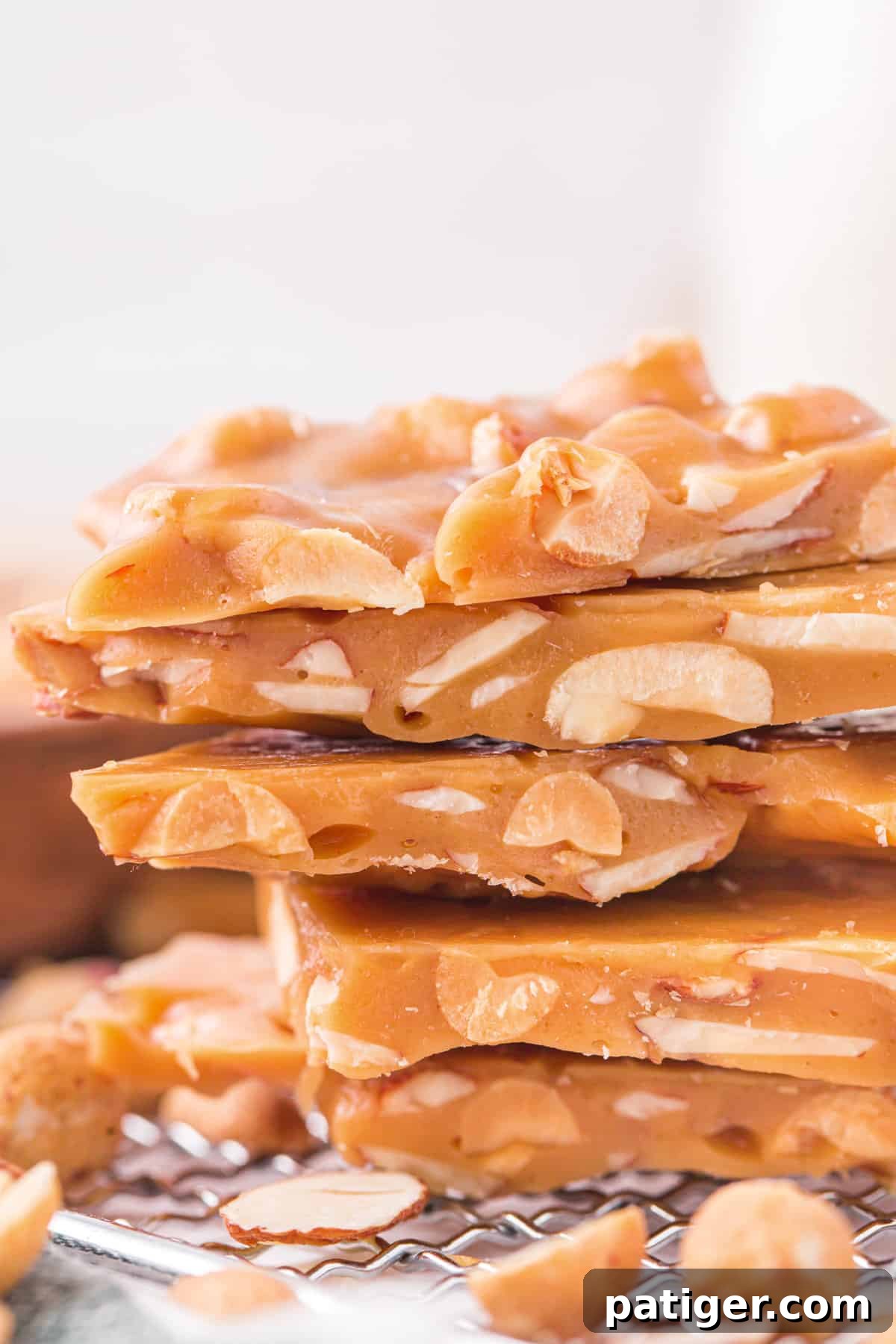 A side view of multiple stacked pieces of homemade nut brittle, clearly showing the distinct layers and embedded chunks of almonds and peanuts, emphasizing its irresistible crunch.