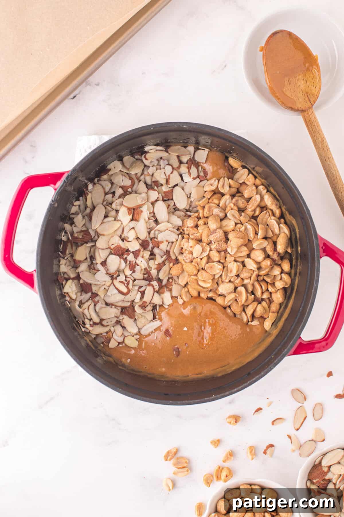 Sliced almonds and salted peanuts being stirred into the hot caramel mixture in the pot, coating them evenly.