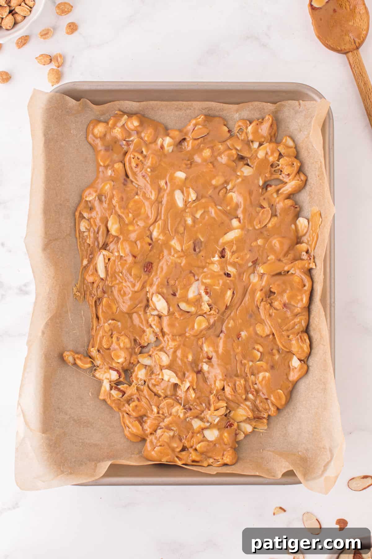 The hot nut brittle mixture freshly poured and spread thinly on a parchment paper-lined baking sheet, with nuts visibly embedded.