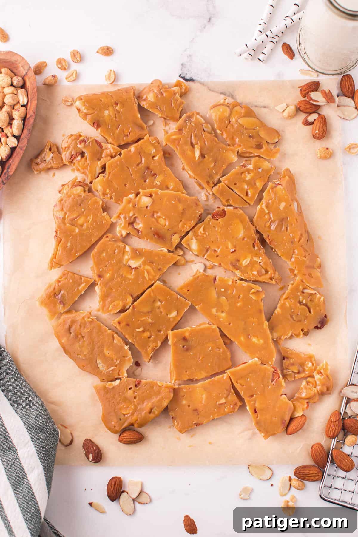Beautifully broken pieces of golden nut brittle, showing the crisp texture and embedded almonds and peanuts, resting on parchment paper.