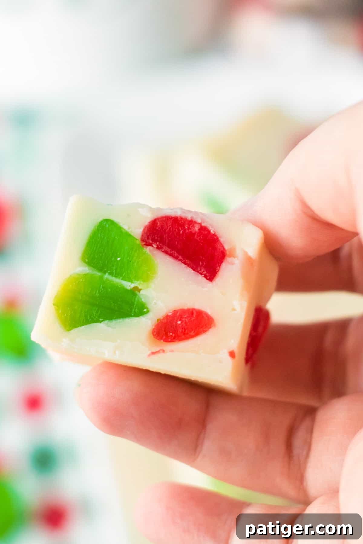 A hand holding a piece of colorful gumdrop fudge, showcasing its vibrant interior.
