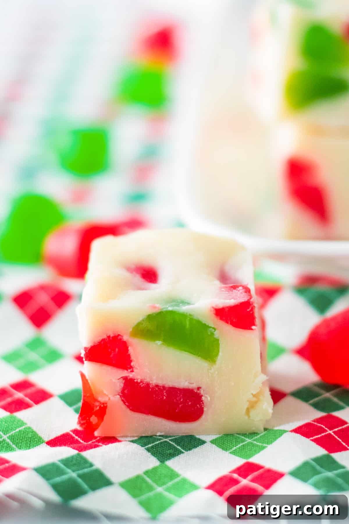 Single piece of gumdrop fudge on a Christmas napkin with a platter of Christmas fudge in the background.