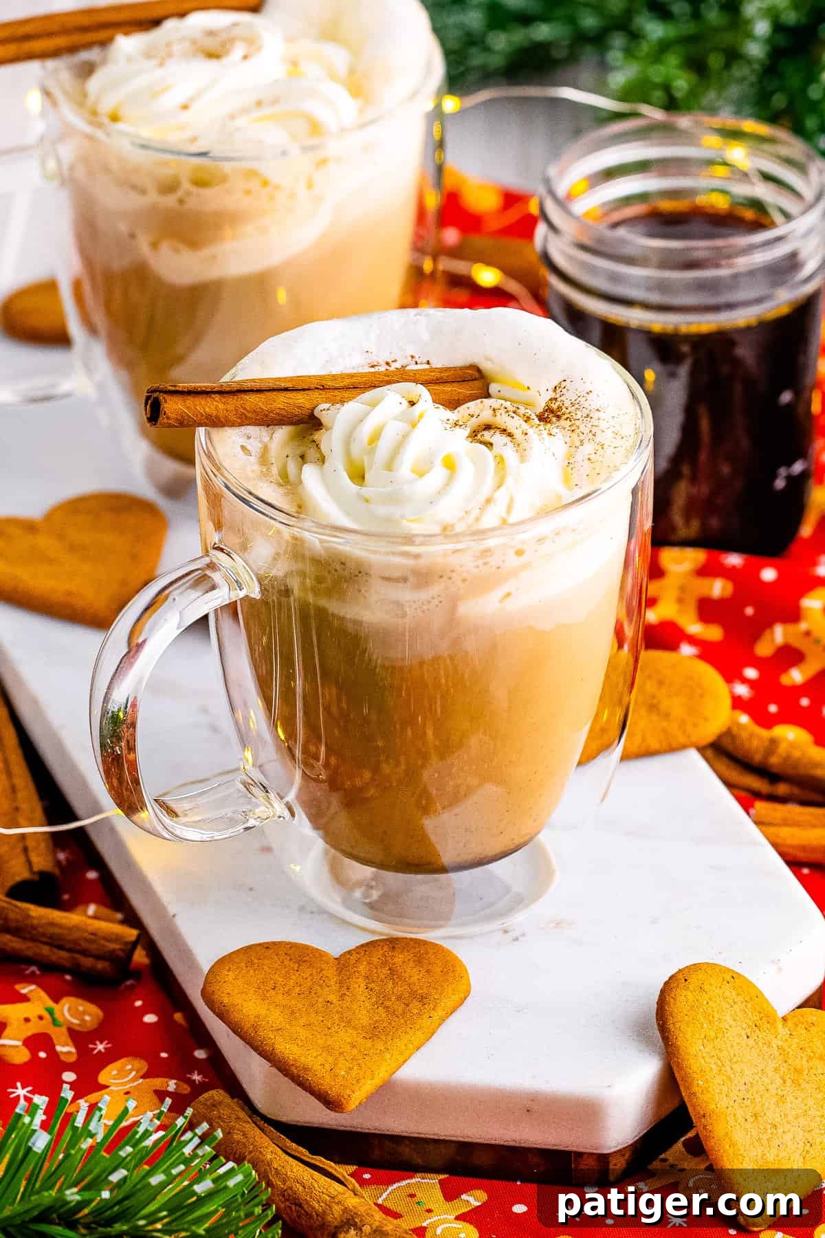 Gingerbread latte surrounded by gingerbread heart cookies, gingerbread syrup in a jar, and Christmas decor.