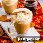 Homemade gingerbread latte in glass mug topped with whipped cream and a cinnamon stick. Heart-shaped gingerbread cookies are next to the hot drink.