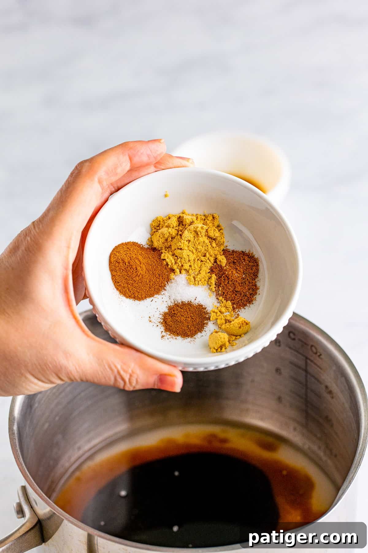 Bowl of spices being added to saucepan.