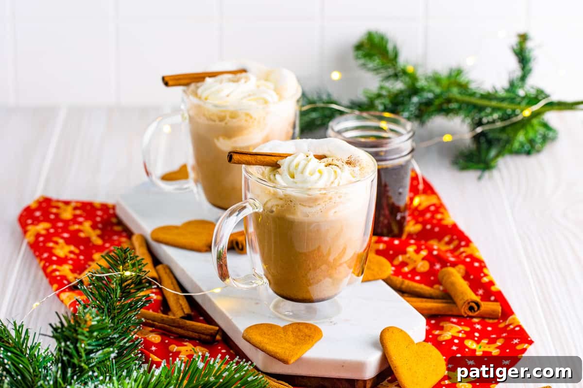 Gingerbread lattes on marble tray topped with whipped cream and cinnamon sticks and surrounded by holiday decor.