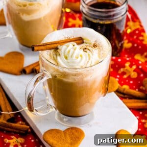 Homemade gingerbread latte in glass mug topped with whipped cream and a cinnamon stick. Heart-shaped gingerbread cookies are next to the hot drink.