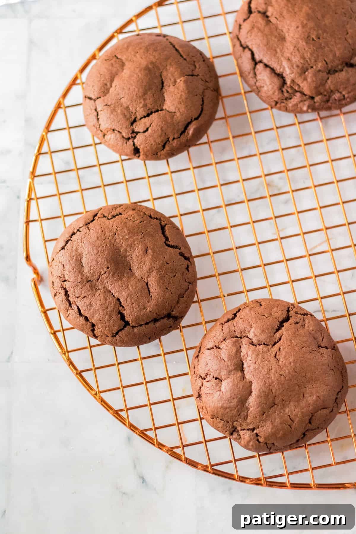 Large, thick chocolate cookies on brass cooling rack.