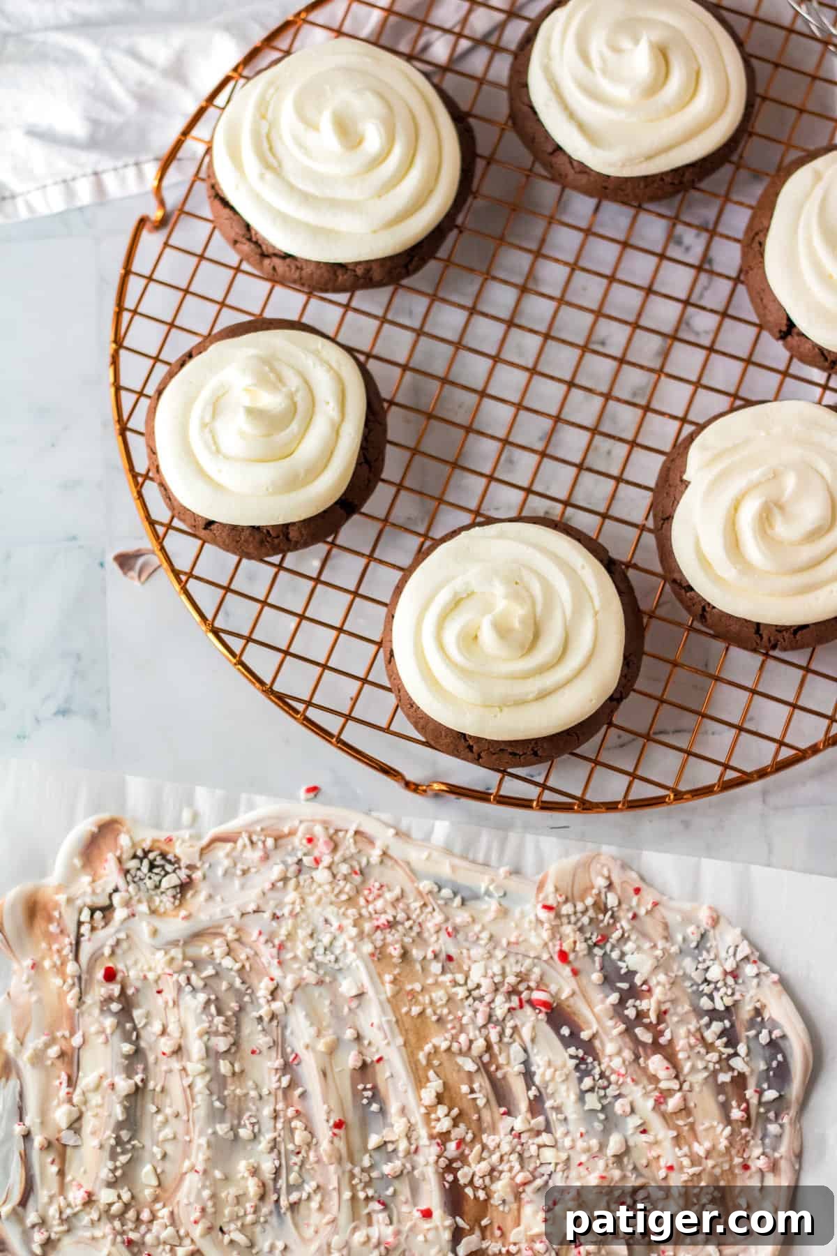 Frosted chocolate cookies on wire rack next to peppermint bark on parchment paper.