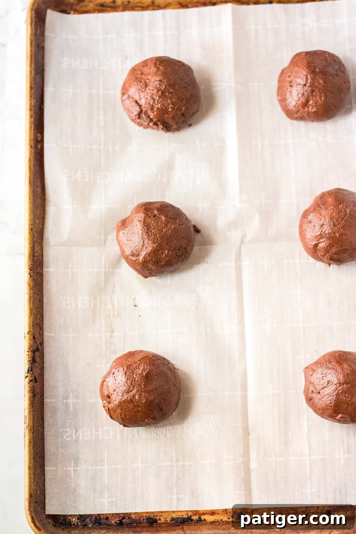 Chocolate cookie dough rolled into large balls on lined cookie sheet.