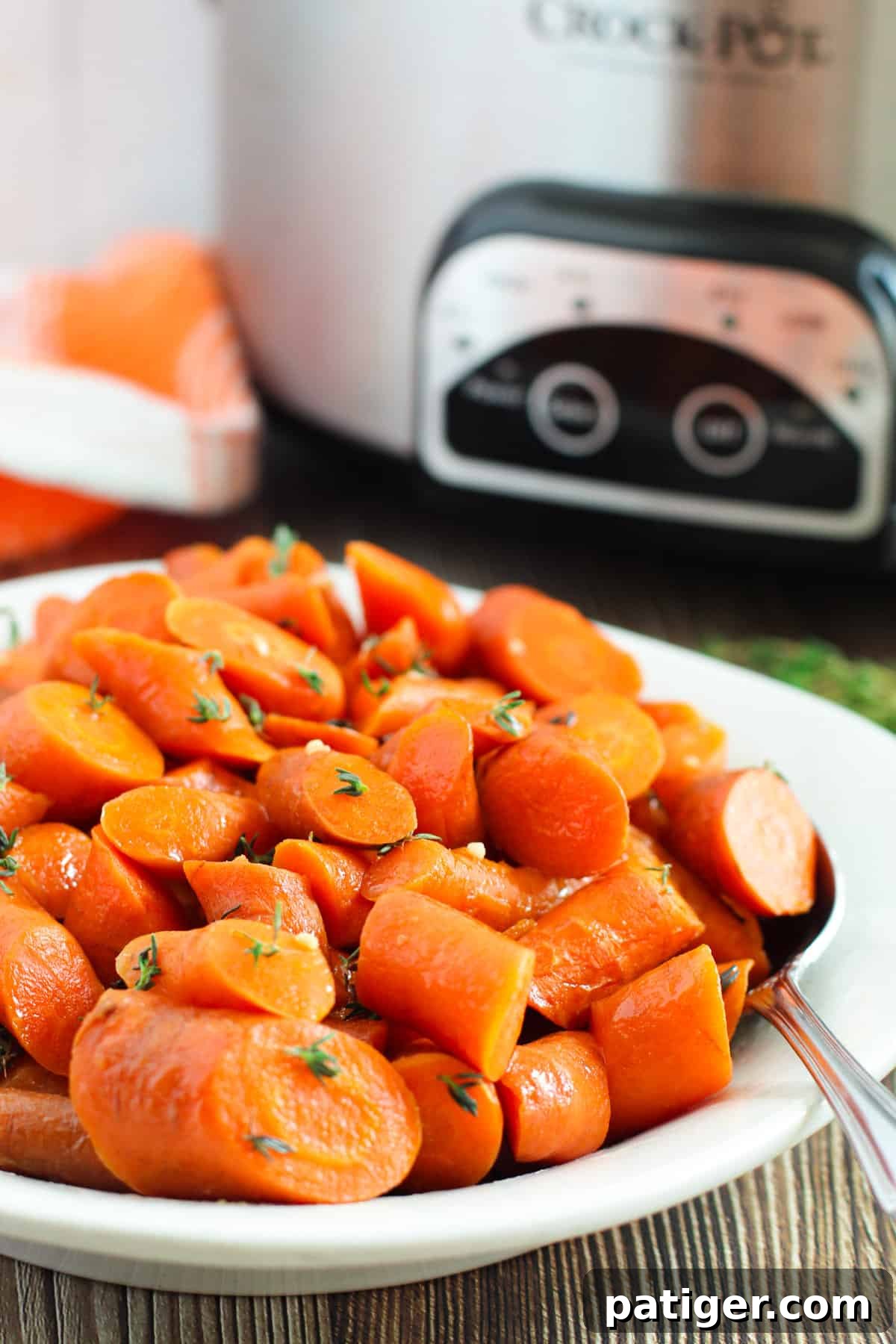Brown sugar glazed carrots artfully arranged with the crockpot visible in the background, highlighting the golden-brown glaze.