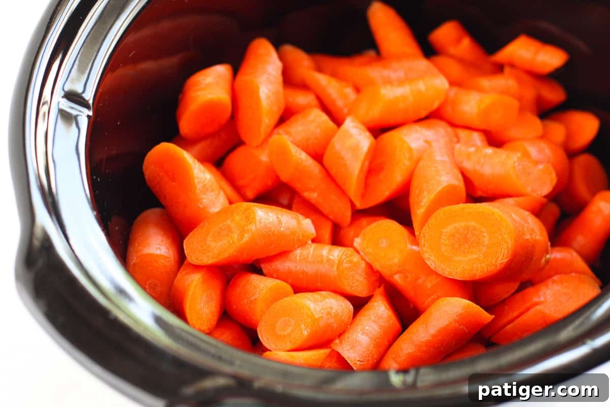 Raw chopped carrots neatly arranged in a crockpot, ready for the glaze.