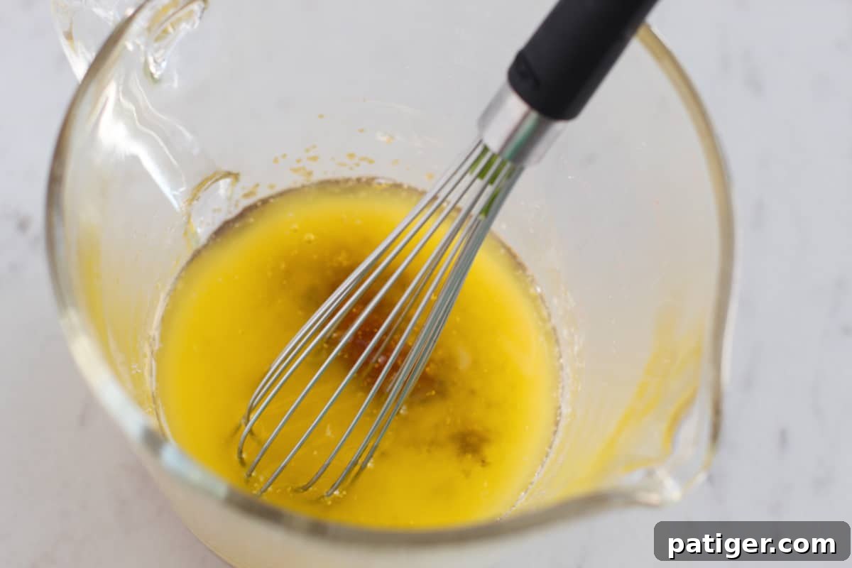 Butter, brown sugar, minced garlic, and salt being whisked together in a glass measuring cup, forming a luscious glaze.