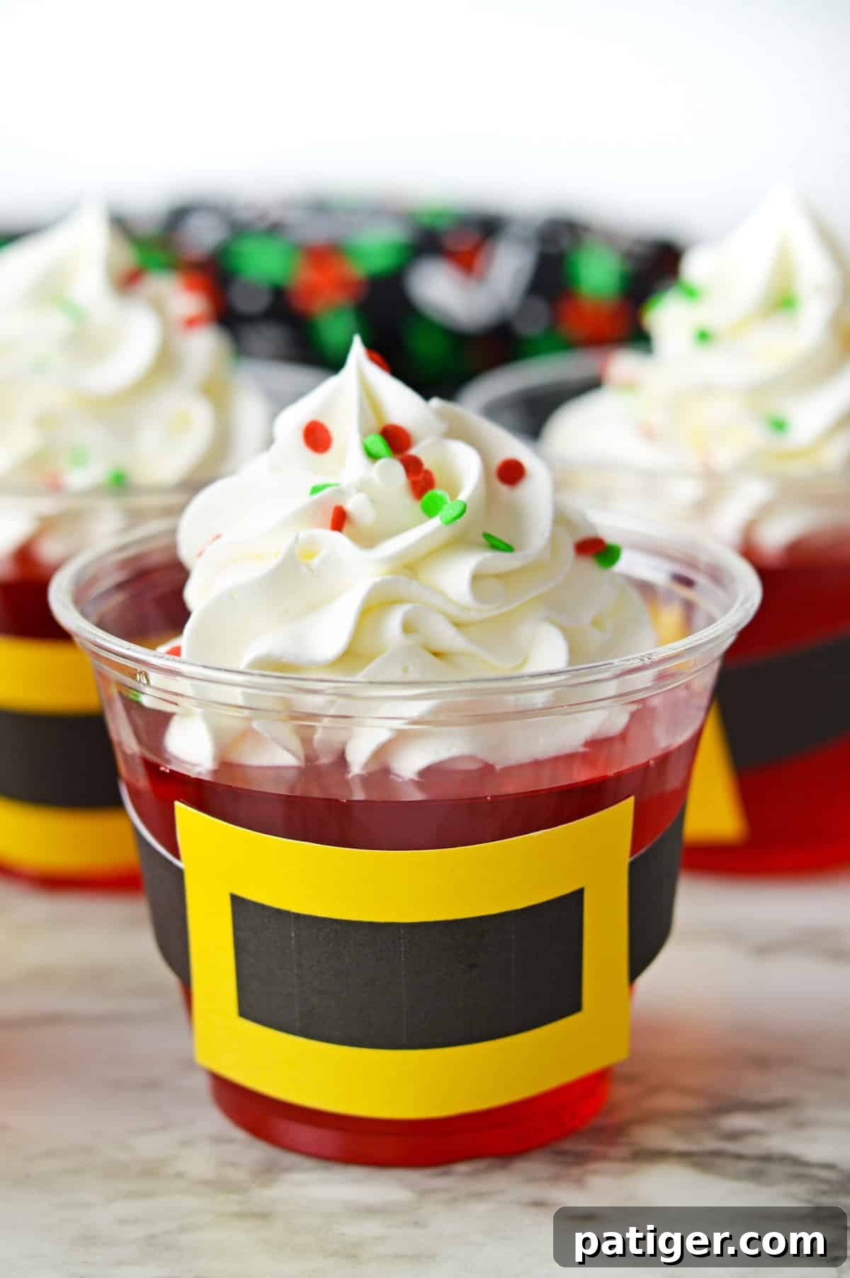 Santa Jello cups with Santa belt printable cut out and taped around the cups, presented on a festive surface.