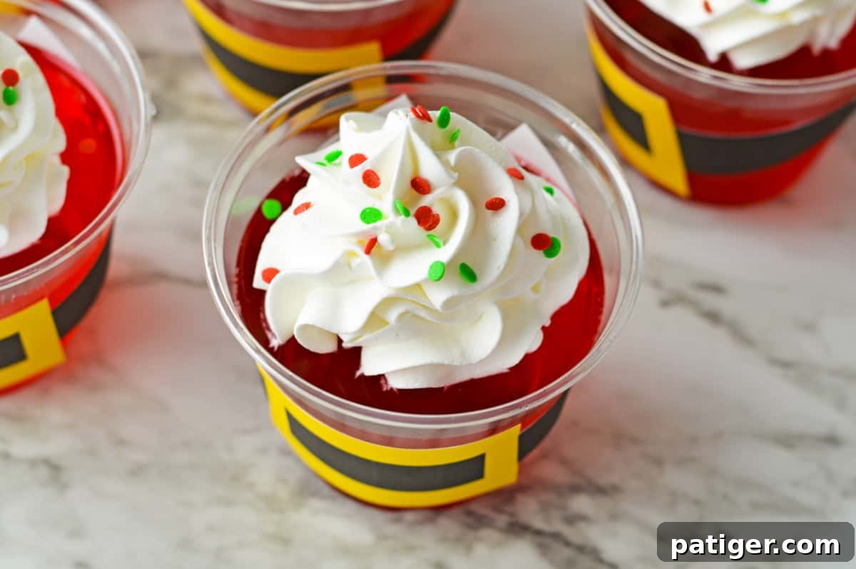 Close-up of a red jello cup topped with a generous swirl of whipped cream and colorful Christmas sprinkles.