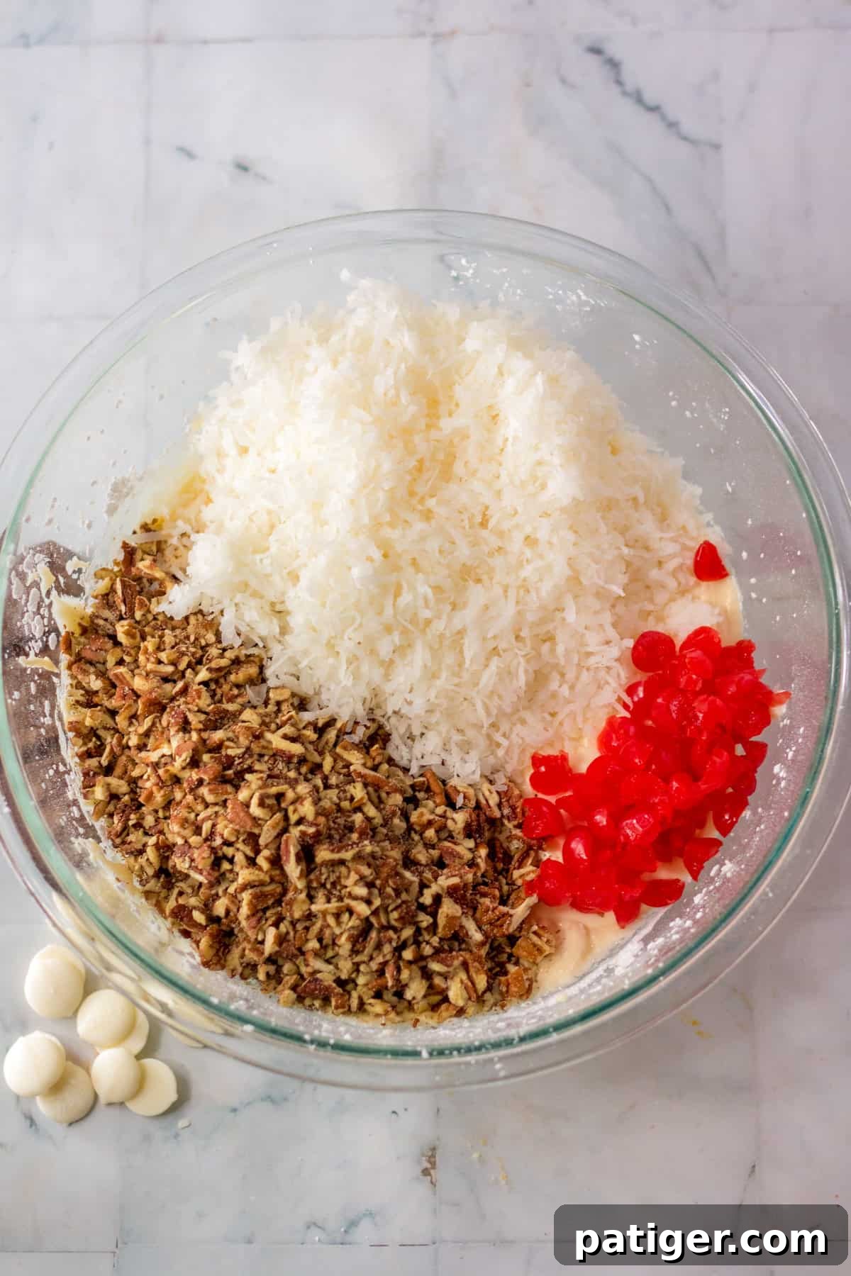 A close-up shot of shredded coconut, chopped pecans, and maraschino cherries being added to the mixing bowl, ready to be incorporated into the candy base.