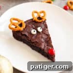 A festive chocolate brownie decorated like an adorable reindeer with pretzel twist antlers, a red M&M nose, and cheerful candy eyes, embodying the holiday spirit.