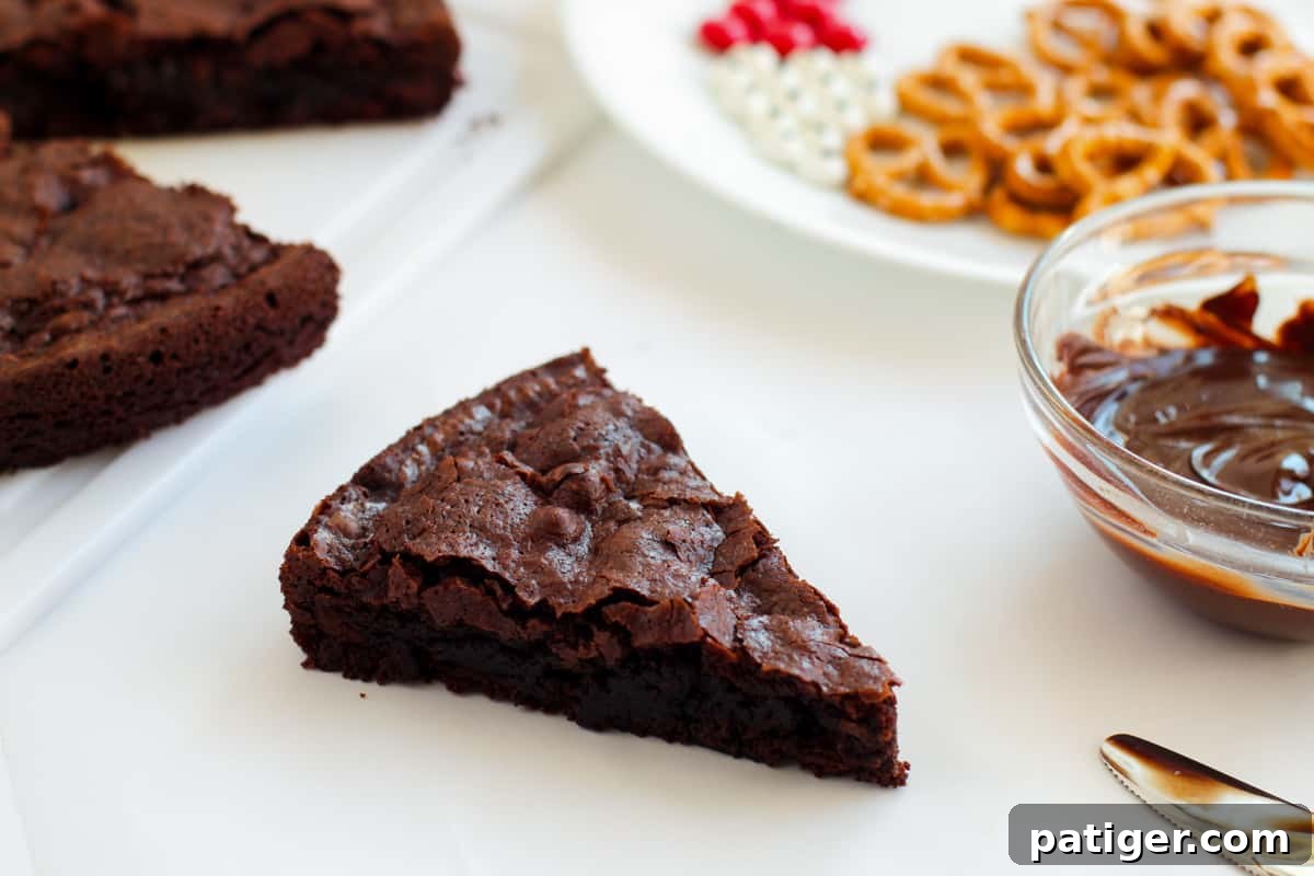 A perfectly sliced triangular brownie, resting on a cutting board, with the remaining round of brownies and decorative candies blurred in the background, ready for assembly.