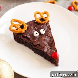 Rich chocolate brownie decorated like an adorable reindeer with crunchy pretzel twist antlers, a vibrant red M&M nose, and playful candy eyes, ready for Christmas celebrations.