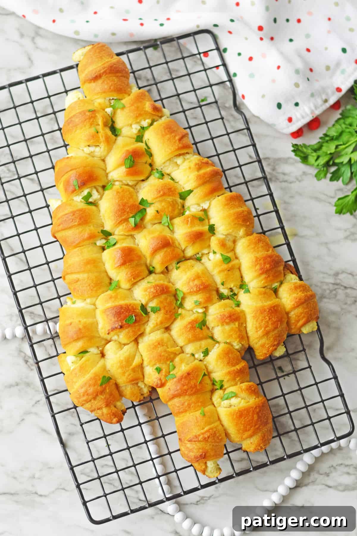 Glistening pull-apart crescent roll Christmas Tree, golden brown and topped with melted butter and fresh parsley, resting on a wire rack.