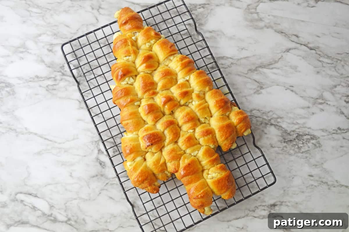A freshly baked, golden brown crescent roll Christmas tree cooling on a wire rack, ready for its final festive touches.
