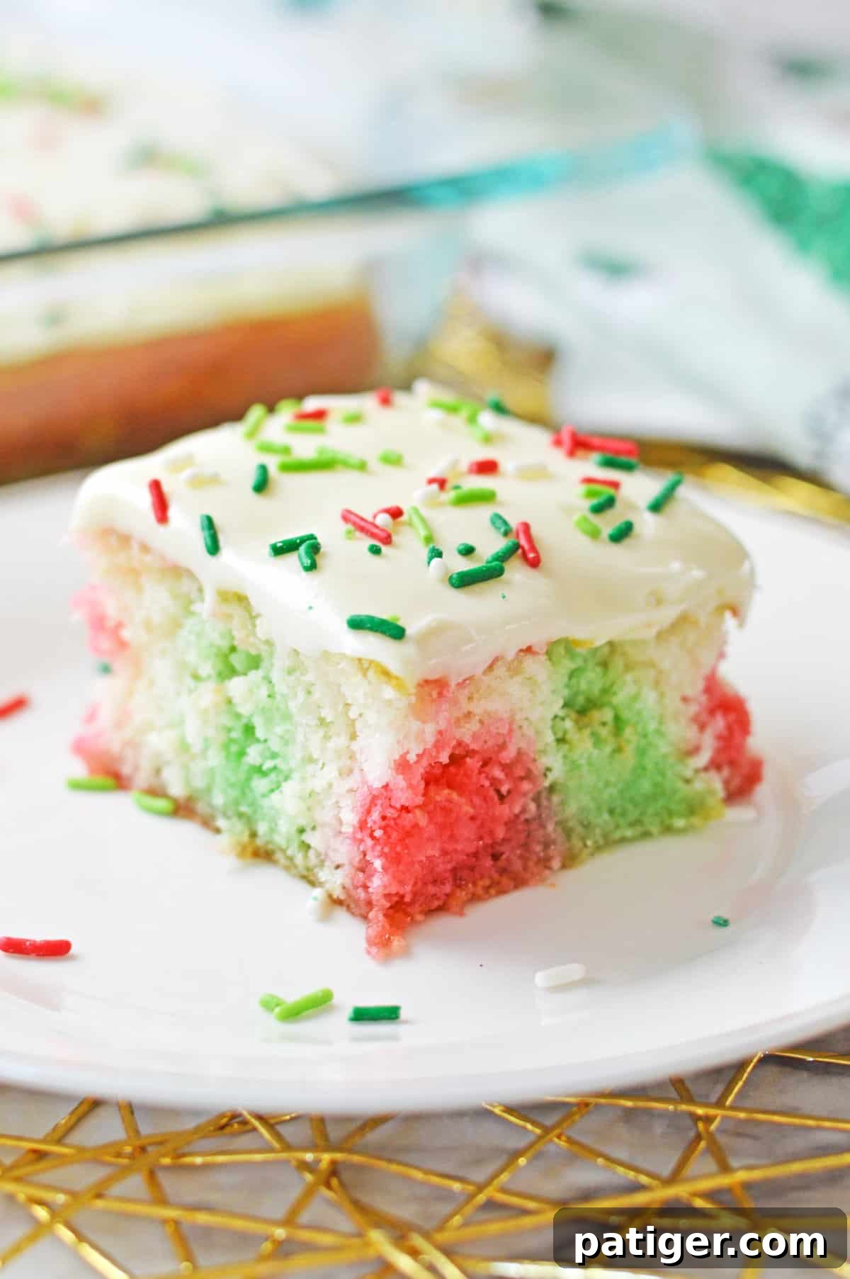 Christmas poke cake with pockets of red and green color throughout a fluffy white sheet cake and vanilla frosting with red and green sprinkles.