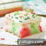 Christmas poke cake with pockets of red and green color throughout a fluffy white sheet cake and vanilla frosting with red and green sprinkles.