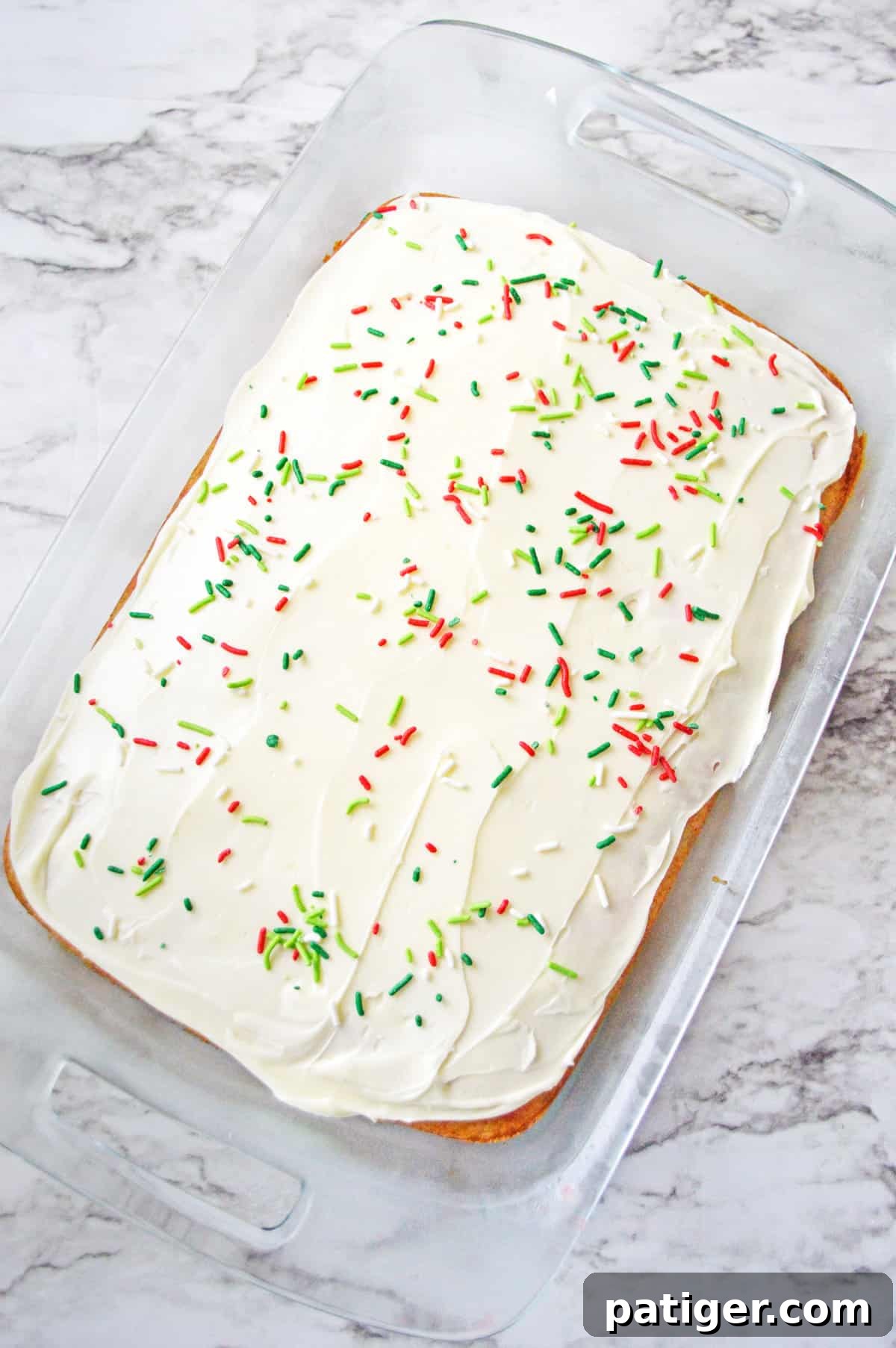 Rectangular cake in 9x13 baking dish topped with vanilla frosting and christmas sprinkles.